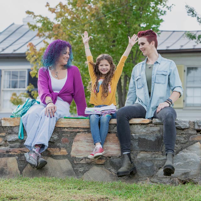 Common Questions- child raising hands between two smiling parents